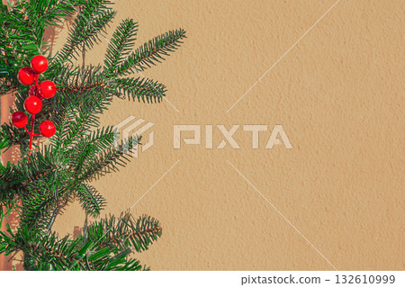 Artificial Christmas tree branches with green needles and bright red berries of symbolic ritual holly are visible against a brown-gray background. Copy space. Artwork template Artificial Christmas tree branches with green needles and bright red berries of symbolic ritual holly are visible against a brown-gray background. Copy space. Artwork template 132610999