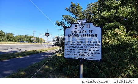 A large metal historical sign informing about the Second Manassas campaign is located in the shade of trees next to the highway and sidewalk on a clear sunny day A large metal historical sign informing about the Second Manassas campaign is located in the shade of trees next to the highway and sidewalk on a clear sunny day 132611394