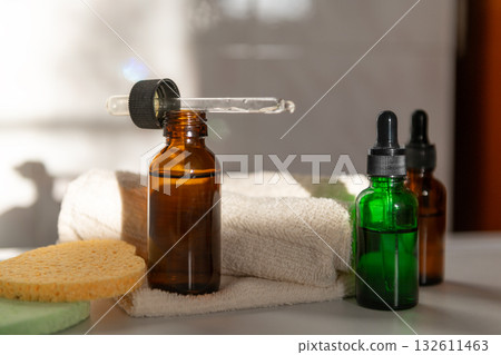 Amber glass dropper bottles with sponge in bathroom with shadows 132611463
