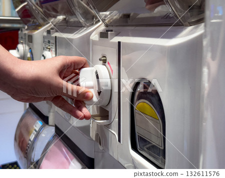 A Person Turns the Handle of a Capsule Toy Vending Machine. Capturing the Joyful Anticipation of a Random Surprise on a Bright Monday Morning. A Person Turns the Handle of a Capsule Toy Vending Machine. Capturing the Joyful Anticipation of a Random Surprise on a Bright Monday Morning. 132611576