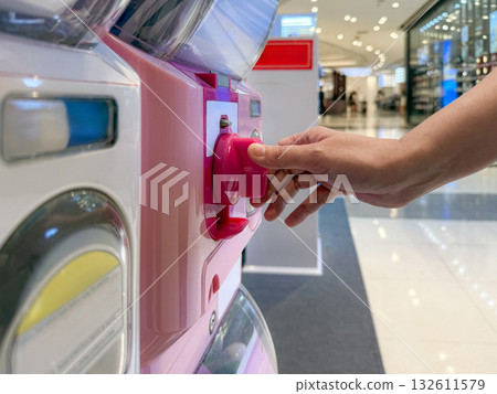 A Person Turns the Handle of a Capsule Toy Vending Machine. Capturing the Joyful Anticipation of a Random Surprise on a Bright Monday Morning. A Person Turns the Handle of a Capsule Toy Vending Machine. Capturing the Joyful Anticipation of a Random Surprise on a Bright Monday Morning. 132611579