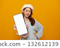 Smartphone mockup blank screen in hand cheerful Asian woman showcasing mobile app on vibrant yellow studio background for advertising and copy space 132612139
