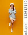 Success celebration happy young Asian woman in cozy sweater raising fists on vibrant yellow studio background full body portrait with copy space for advertising 132612140