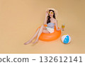 Summer vacation travel woman relaxing on orange inflatable ring holding cocktail beside beach ball on beige studio background with copy space ideal for travel ads and lifestyle mockups 132612141