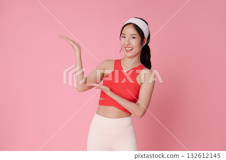 Fitness asian woman presenting copy space on pink background in red sports top for wellness advertising gym promotion and healthy lifestyle banner mockup Fitness asian woman presenting copy space on pink background in red sports top for wellness advertising gym promotion and healthy lifestyle banner mockup 132612145