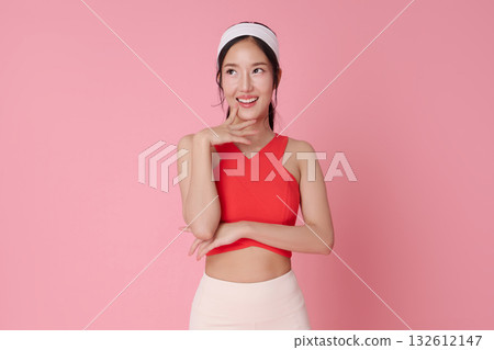 Fitness model Asian woman on pink background in red sports top smiling thinking for wellness and active lifestyle athleisure advertising 132612147