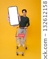 Full length happy Asian man showing smartphone mockup blank screen application shopping trolley promotion supermarket isolated on yellow background. 132612158