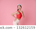 Fitness model Asian woman in red sports top smiling on pink background for wellness, active lifestyle and athleisure advertising with copy space 132612159