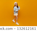 Happy Asian woman walking on yellow background wearing blue sweater and beret lifestyle fashion portrait with copy space for social media advertising youth branding and positive campaigns 132612161