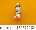 Jumping woman on yellow background, cheerful Asian girl in blue sweater and beret leaping midair copy space for fashion, lifestyle, youth, happiness, promotion, and social media banner. 132612162