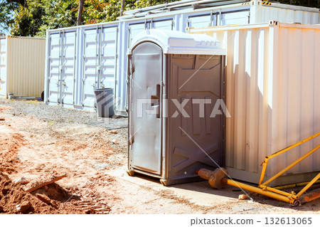 Portable restroom is located next to shipping containers at busy construction area Portable restroom is located next to shipping containers at busy construction area 132613065