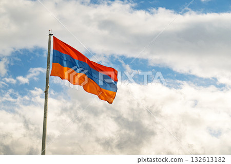 A flag with the colors red and orange is flying in the sky 132613182