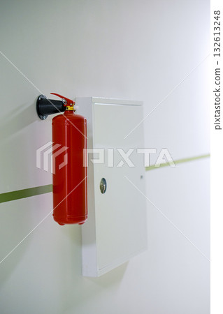 A red fire extinguisher is hanging on a white wall A red fire extinguisher is hanging on a white wall 132613248