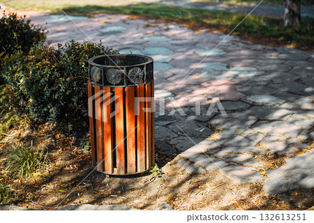 A trash can is sitting on a sidewalk in front of some bushes 132613251