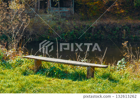 A wooden bench sits in a grassy field next to a river 132613262