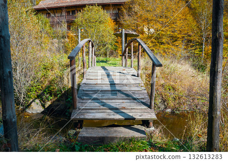 A wooden bridge over a stream with a house in the background A wooden bridge over a stream with a house in the background 132613283