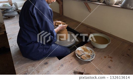 Back view of a man making pottery using a potter's wheel 132613614