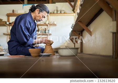 Senior man shaping pottery using a potter's wheel 132613620