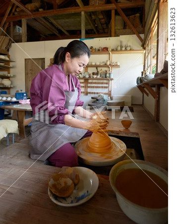 A woman making pottery using a potter's wheel 132613623