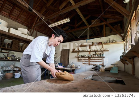 陶藝工作室裡,一位年輕男子正在揉捏陶土。 陶藝工作室裡,一位年輕男子正在揉捏陶土。 132613743