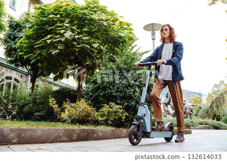 Man riding electric scooter in park surrounded by trees on a sunny day 132614033