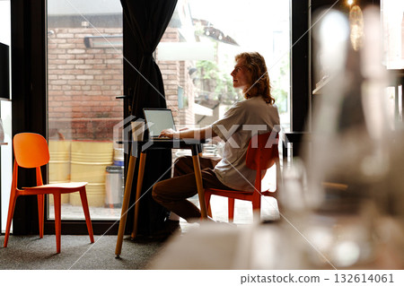 Young man working on a laptop in a cozy cafe with modern decor Young man working on a laptop in a cozy cafe with modern decor 132614061