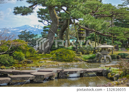 The beauty of the winter garden at Kenrokuen Garden in Kanazawa, with the Ganko Bridge and Kishin lanterns, and the snow-capped Mount Io in the distance 132616035