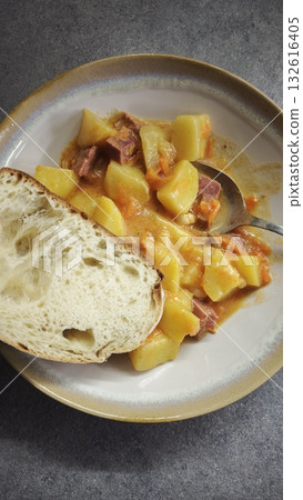 Plate of homemade stewed potatoes with meat and vegetables served with a slice of bread. The image conveys the concept of comfort food and traditional homemade meal 132616405