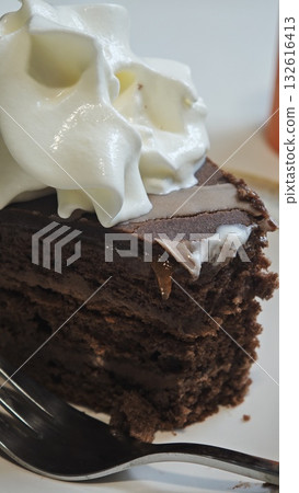 Slice of rich chocolate cake with whipped cream topping served on a plate. The image conveys the concept of indulgence, celebration, and sweet dessert pleasure 132616413