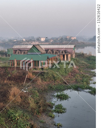 An abandoned, partially constructed building sits amidst overgrown vegetation and water, suggesting neglect and the passage of time 132616422