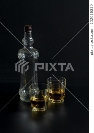 A bottle of liquor and two glasses of liquor on a table 132616839