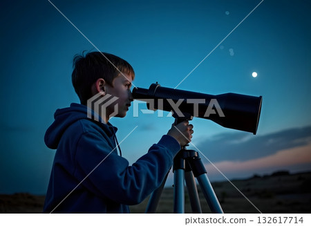 Close up face of curious kid child using telescope to explore moon surface. Little boy stargazing at night with a telescope to see galaxy from his room decorated bedroom with rocket in background. 132617714