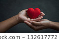 A pair of hands gently cradling a red heart representing love, compassion, care and kindness against a soft, neutral backdrop. 132617772