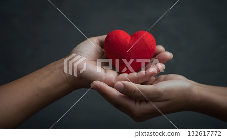 A pair of hands gently cradling a red heart representing love, compassion, care and kindness against a soft, neutral backdrop. A pair of hands gently cradling a red heart representing love, compassion, care and kindness against a soft, neutral backdrop. 132617772