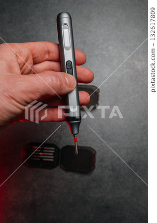 Technician fixing electronic device, Closeup of hand using cordless screwdriver, Focused technician repairing electronics with magnetic bit and red indicator light Technician fixing electronic device, Closeup of hand using cordless screwdriver, Focused technician repairing electronics with magnetic bit and red indicator light 132617809