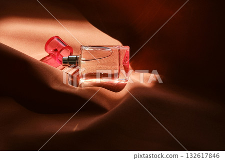 A pink perfume bottle on a soft reddish background. A pink perfume bottle on a soft reddish background. 132617846