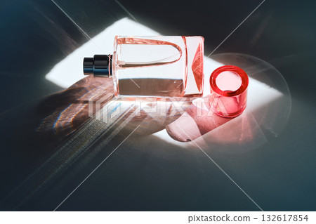 Pink perfume bottle on the light background in the rays of sun with highlights. 132617854