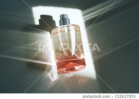 Pink perfume bottle on the light background in the rays of sun with highlights. Pink perfume bottle on the light background in the rays of sun with highlights. 132617855