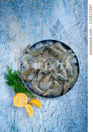 Fresh raw shrimp spread on ice with lemon and cilantro slices on a marble surface, ready to cook, no people Fresh raw shrimp spread on ice with lemon and cilantro slices on a marble surface, ready to cook, no people 132617887