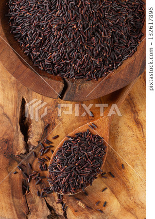 Natural black rice in a wooden bowl and spoon on a wooden surface in rustic style, top view 132617896