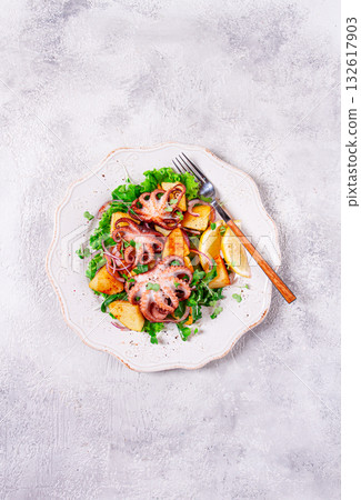 Grilled octopus with baked potatoes and fresh herbs, on a decorative light plate, homemade, no people 132617903