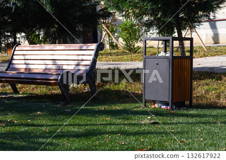 Park bench and waste bin located in a neatly maintained green space on a sunny day Park bench and waste bin located in a neatly maintained green space on a sunny day 132617922