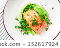 Grilled salmon filet served on a bed of green pea puree with fresh microgreens and peas, presented on a white plate 132617924