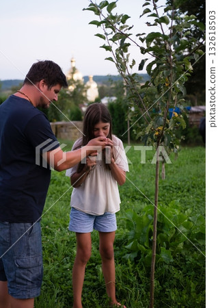 A father and daughter enjoy a moment together in a garden, examining a small tree. A father and daughter enjoy a moment together in a garden, examining a small tree. 132618503