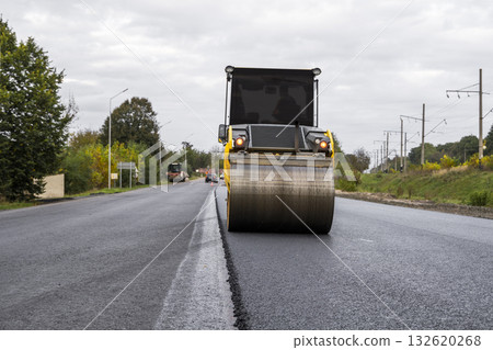 Yellow asphalt roller smoothing new road surface during roadworks on rural highway 132620268