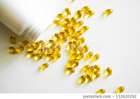 Golden vitamins spilled from white bottle on bright surface Golden vitamins spilled from white bottle on bright surface 132620292