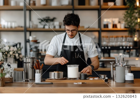 A male barista carefully prepares a creamy beverage behind the counter of his modern cafe A male barista carefully prepares a creamy beverage behind the counter of his modern cafe 132620843