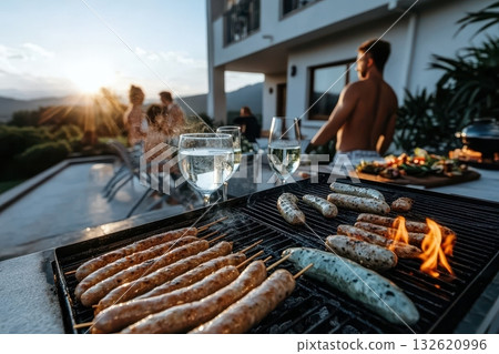 Friends enjoy a sunset barbecue, grilling sausages and drinking wine by the pool 132620996