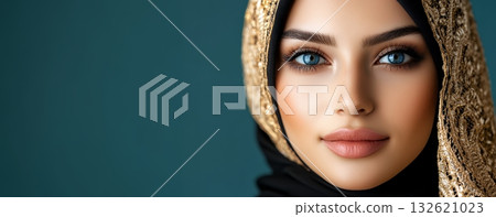 Beautiful woman with striking blue eyes, wearing a black hijab with gold embroidery, poses against a teal backdrop Beautiful woman with striking blue eyes, wearing a black hijab with gold embroidery, poses against a teal backdrop 132621023