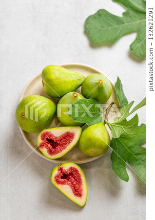 Sweet green figs on a plate, sliced, with leaves on a light background. 132621291